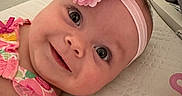 Avalynn is registered to the contest to win money with this photo: baby, child, close_up, colorful_clothing, cute, eyes, face, flower, happy, headband, indoors, infant, lying_down, person, pink, portrait, skin, smiling, soft_lighting, texture