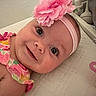 baby, smiling, headband, flower, pink, colorful_clothing, face, child, infant, close_up, portrait, happy, cute, lying_down, skin, eyes, indoors, soft_lighting, texture, person