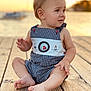 baby, beachwear, bodypart, clothing, dress, face, finger, hand, head, nature, outdoors, pants, person, photography, portrait, shorts, sitting, water, waterfront, wood