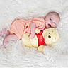 baby, baby_clothes, child, comfort, cozy, cute, happy, infant, lying_down, peach_outfit, plush_toy, portrait, smiling, soft_rug, soft_texture, stuffed_animal, toddler, toy, white_background, winnie_the_pooh