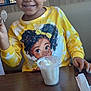 Ava is registered to the contest to win money with this photo: child, smiling, curly_hair, yellow_shirt, cartoon_print, spoon, ice_cream, table, restaurant, tray, fries, ketchup, window, daylight, happy, food, indoor, person, cute, portrait