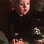 baby, child, indoor, black_clothing, headband, bow, patterned_leggings, orange_socks, carpet, curious_expression, sitting, hand, face, person, infant, young_child, cute, looking_away, cozy, dim_lighting