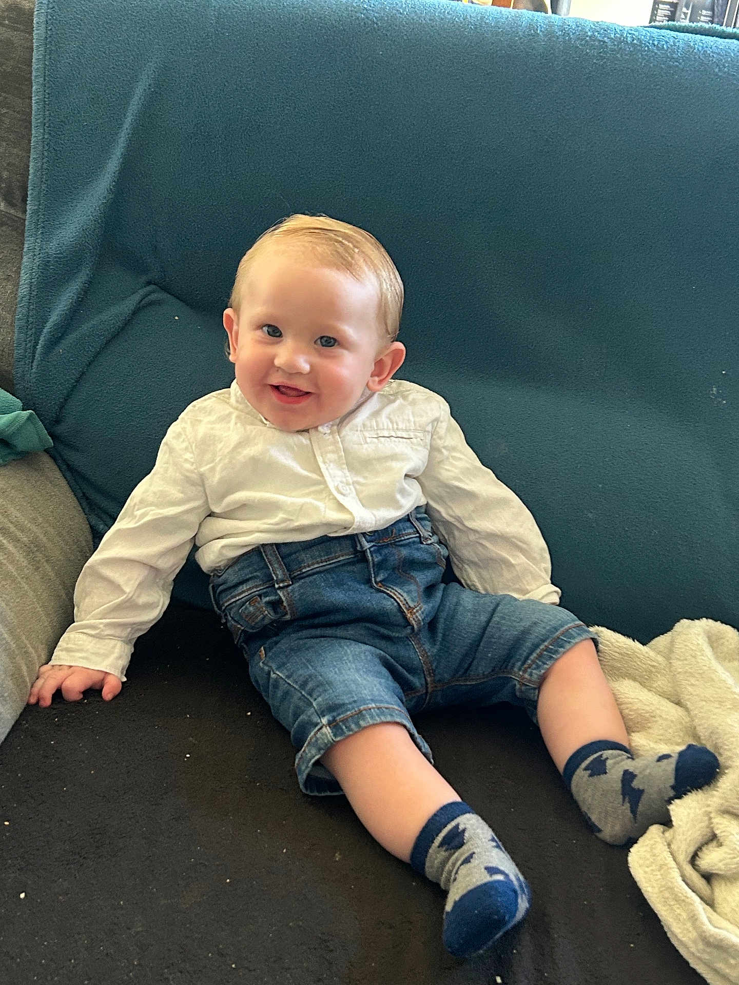 Tiago a rejoint le concours — aidez-le/la à gagner de superbes lots ! baby, child, smiling, sitting, couch, denim_shorts, white_shirt, socks, blanket, indoor, happy, cute, young_child, face, person, comfortable, relaxed, home, casual, playful