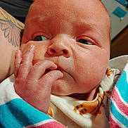 Dominic is registered to the contest to win money with this photo: baby, blanket, close_up, clothing, curious, cute, expression, face, fingers, hand, indoors, infant, newborn, person, portrait, skin, sleepy, tattoo, wrapped, young