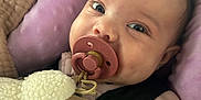 Mariah is registered to the contest to win money with this photo: baby, pacifier, plush_toy, sheep, pink_cushion, close_up, infant, child, soft_toy, cozy, cute, clothing, hand, face, seatbelt, indoors, portrait, young_child, smiling, curious