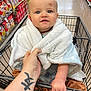 baby, shopping_cart, blanket, grocery_store, aisle, snacks, hand, tattoo, blue_eyes, infant, clothing, floor, person, holding, cute, portrait, shopping, child, cart, wrapped