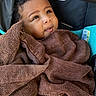 baby, child, towel, brown, curly_hair, stroller, blanket, face, portrait, infant, cute, wrapped, cozy, looking_up, indoors, soft_texture, person, young, comfortable, expression