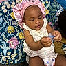 Princess is registered to the contest to win money with this photo: baby, infant, pacifier, pink_bonnet, white_clothing, floral_cushion, pattern, indoor, child, cute, sitting, looking_down, hand, headwear, soft_lighting, skin_tone, fabric, comfort, portrait, young_child