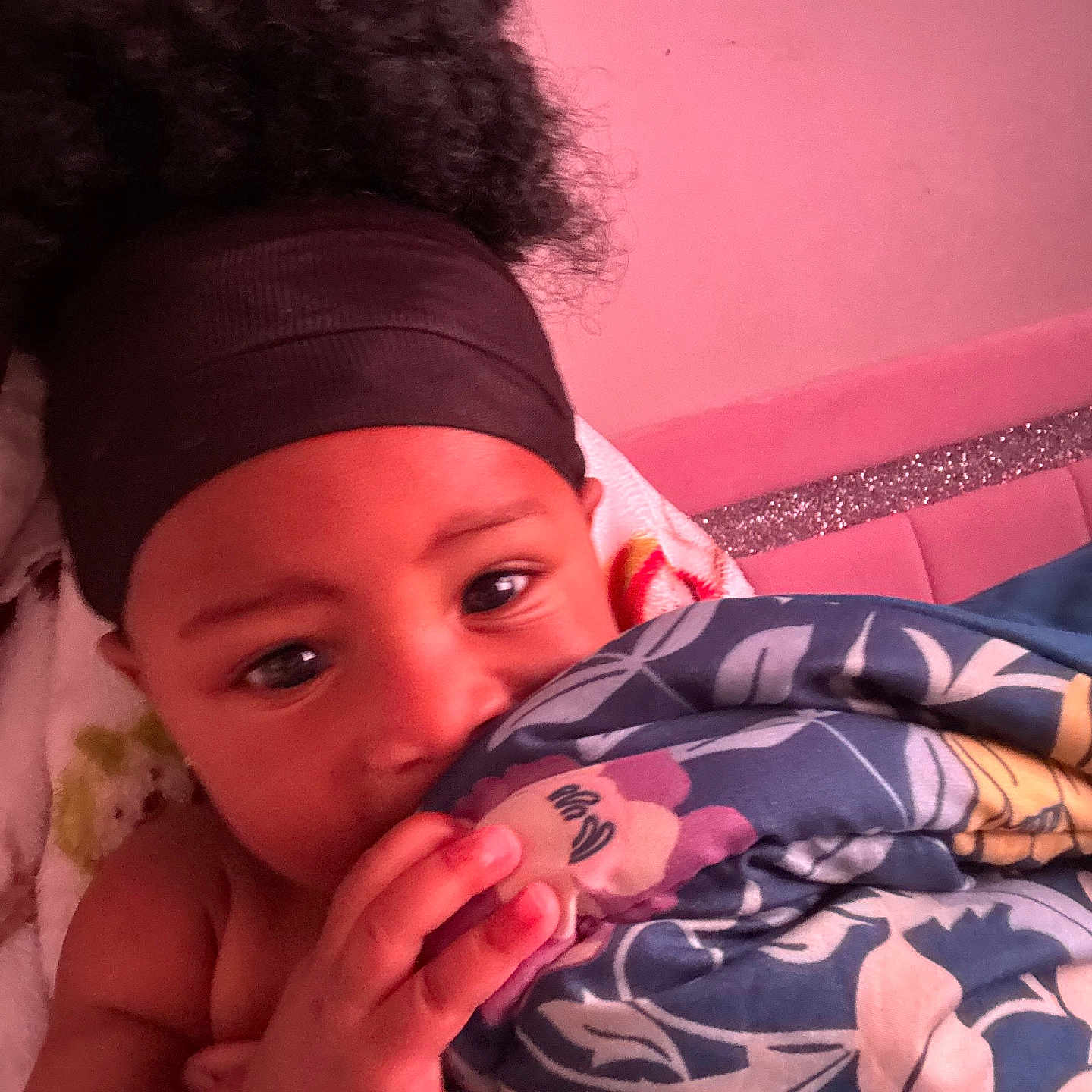 Princess is registered to the contest to win money with this photo: baby, child, blanket, headband, face, hand, indoor, pink_wall, glitter, curly_hair, toddler, portrait, cozy, bedroom, cute, looking_at_camera, wrapped, soft_lighting, young_child, infant