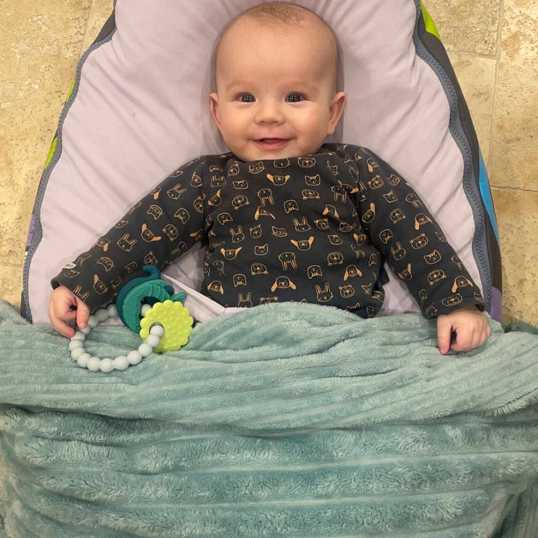 Mylan a rejoint le concours — aidez-le/la à gagner de superbes lots ! baby, baby_seat, blanket, child, clothing, comfort, cozy, cute, floor, happy, indoor, infant, person, portrait, smiling, soft, teething_toy, tile, toy, wrapped