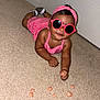 Araiya Lynn joined the competition — help win amazing prizes! baby, child, pink_clothing, sunglasses, headband, carpet, snack, star_shaped, indoors, cute, smiling, hand, footwear, fashion, person, playful, lying_down, food, accessory, happy