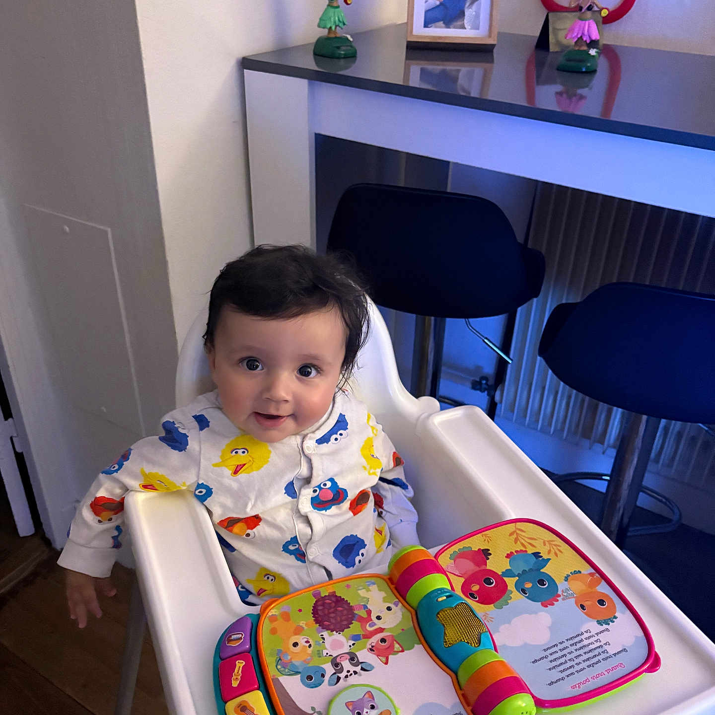 Chaieb Noah participe au concours pour gagner de l'argent avec cette photo : baby, book, child, colorful, counter, face, family_photo, figurines, furniture, happy, high_chair, indoor, kitchen, pajamas, person, playtime, sesame_street, smile, toy, wooden_floor