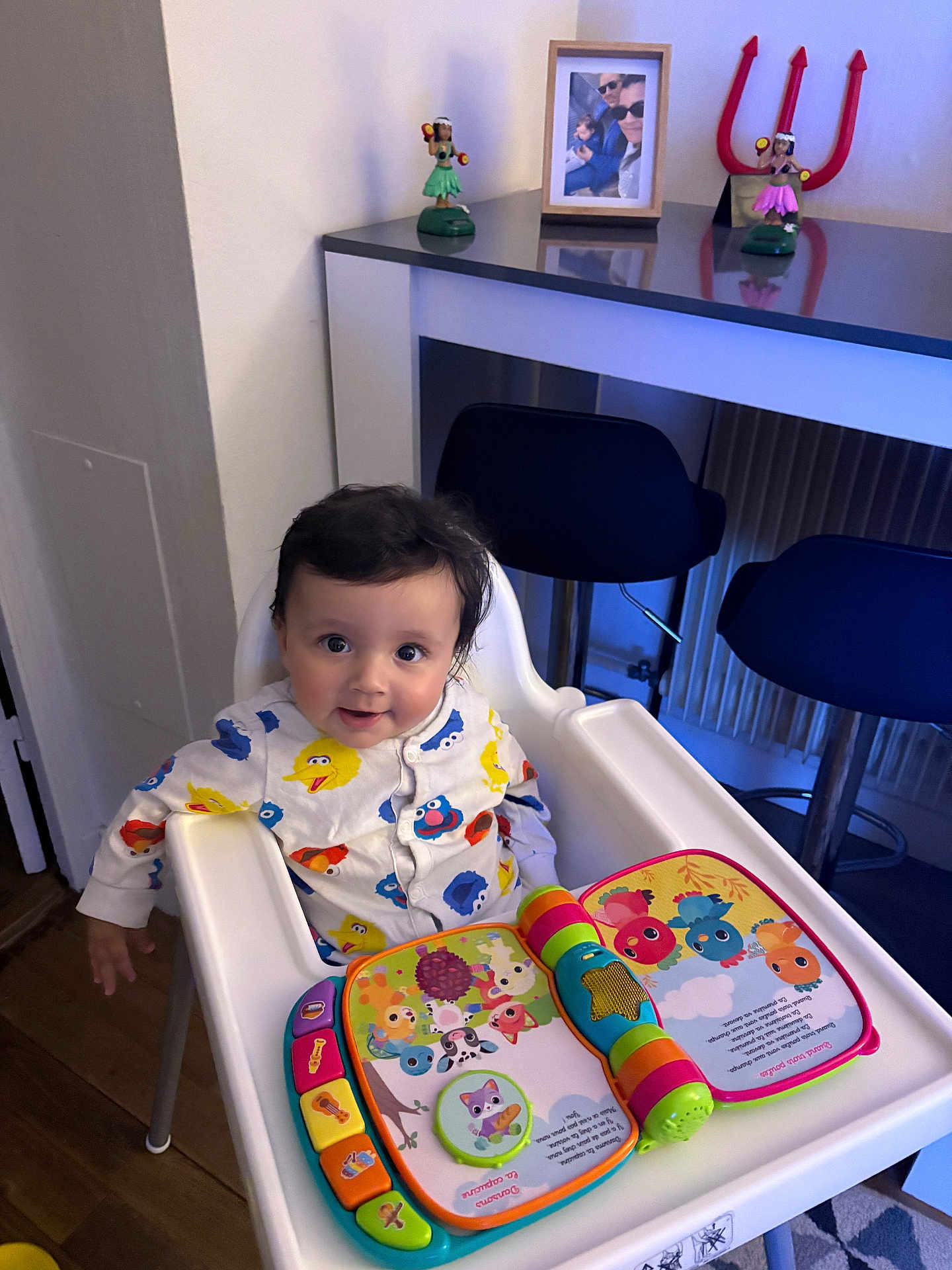 Chaieb Noah participe au concours pour gagner de l'argent avec cette photo : baby, high_chair, toy, book, pajamas, sesame_street, colorful, face, smile, indoor, wooden_floor, kitchen, counter, figurines, family_photo, child, person, furniture, happy, playtime