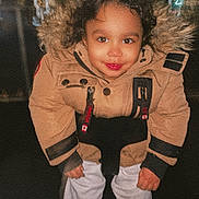 Lorenzo is registered to the contest to win money with this photo: child, toddler, jacket, fur_hood, swing, night, smile, happy, outdoor, playground, clothing, person, face, dark_background, curly_hair, white_pants, boots, portrait, park, fun