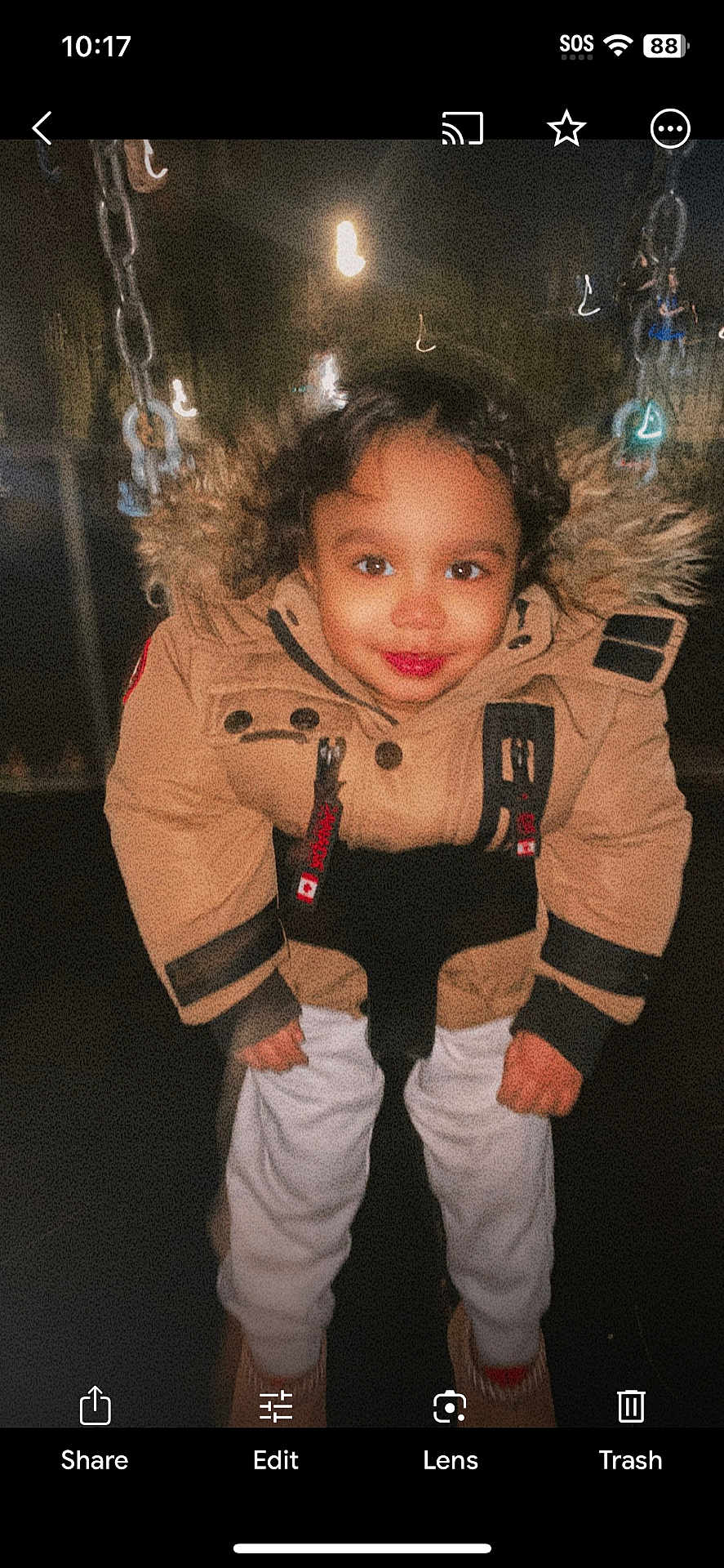 Lorenzo is registered to the contest to win money with this photo: child, toddler, jacket, fur_hood, swing, night, smile, happy, outdoor, playground, clothing, person, face, dark_background, curly_hair, white_pants, boots, portrait, park, fun