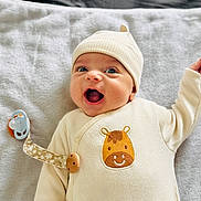 Jed participe au concours pour gagner de l'argent avec cette photo : baby, infant, smiling, cream_clothing, giraffe_patch, pacifier, blanket, happy, cute, child, lying_down, warm_clothing, hat, indoors, close_up, portrait, baby_girl, baby_boy, soft_texture, comfort