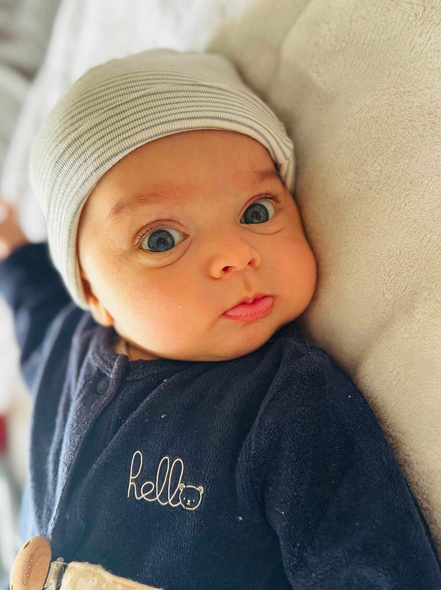 Jed a rejoint le concours — aidez-le/la à gagner de superbes lots ! baby, infant, face, beanie, clothing, onesie, blue_eyes, expression, cute, portrait, soft_texture, laying_down, closeup, child, newborn, headwear, fabric, person, indoors, casual