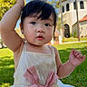 baby, child, dress, pink_bow, outdoor, grass, sunny, park, blanket, curious, raising_hand, face, person, young_child, daylight, smiling, cute, portrait, nature, building
