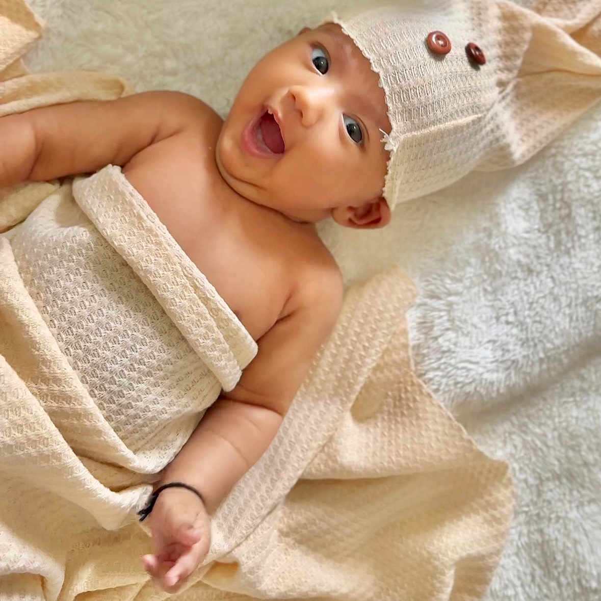 Nirvi joined the competition — help win amazing prizes! baby, blanket, buttons, child, cozy, cute, expression, happy, hat, indoors, infant, lying_down, portrait, skin, smiling, soft_texture, towel, warm, wrapped, young_child