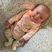 Sierra is registered to the contest to win money with this photo: baby, infant, child, blanket, soft_texture, pink_clothing, smile, lying_down, cute, cozy, warm, face, footwear, patterned_pants, newborn, indoors, comfort, portrait, human, small_hands