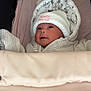 baby, infant, hat, clothing, blanket, face, portrait, cute, smile, indoors, cozy, striped_clothing, white_hat, newborn, child, person, soft_toys_pattern, hood, warm, sleeping_bag