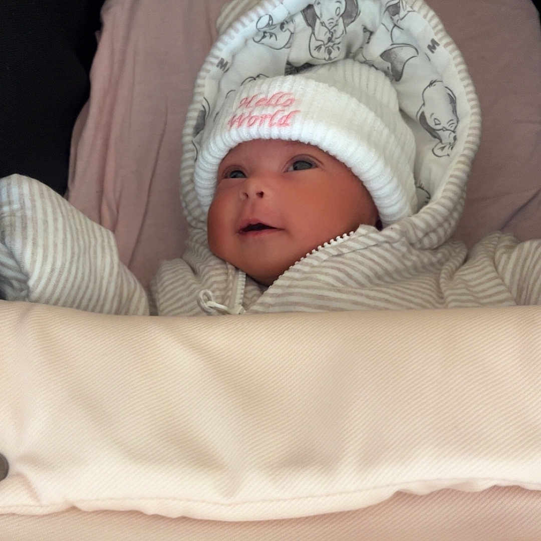 Ocean is registered to the contest to win money with this photo: baby, blanket, child, clothing, cozy, cute, face, hat, hood, indoors, infant, newborn, person, portrait, sleeping_bag, smile, soft_toys_pattern, striped_clothing, warm, white_hat