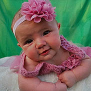 Madison is registered to the contest to win money with this photo: baby, infant, pink, headband, flower, knitted_clothing, blanket, green_background, cute, portrait, smiling, chubby_cheeks, toddler, soft_texture, curious_expression, closeup, child, young, indoors, hands