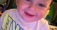Beau is registered to the contest to win money with this photo: baby, blond_hair, blue_eyes, child, close_up, clothing, drool, face, graphic_t_shirt, happy, home, indoor, infant, photography, playful, portrait, rosy_cheeks, sitting, smiling, warm_lighting
