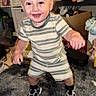baby, blond_hair, box, child, face, furniture, happy, home, indoors, living_room, pajamas, portrait, rug, shelves, smiling, sneakers, standing, striped_clothing, toddler, toy