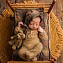 newborn, baby, sleeping, knitted_outfit, bear_ears, teddy_bear, miniature_bed, plaid_blanket, wooden_floor, fringed_rug, cozy, cute, infant, portrait, resting, soft_lighting, warm_tones, child, adorable, peaceful
