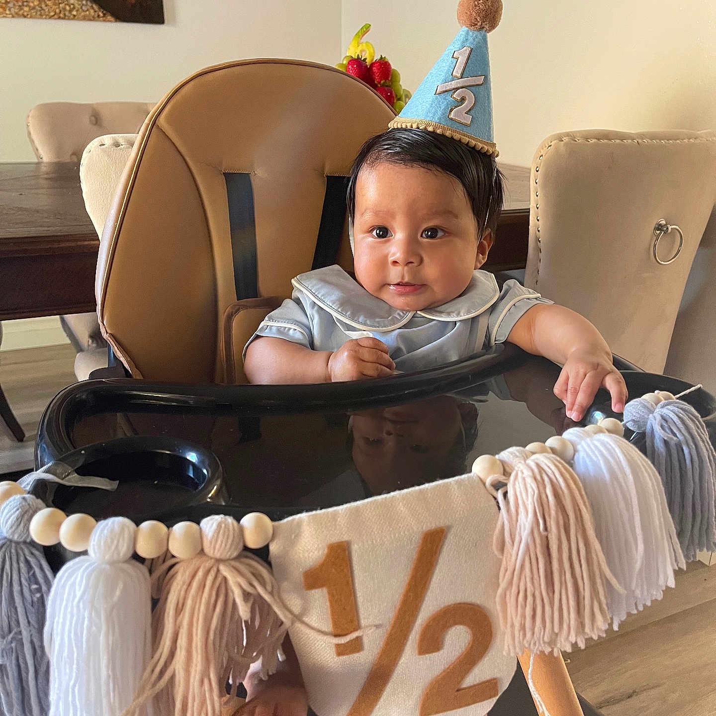 Ryan is registered to the contest to win money with this photo: baby, banner, celebration, chair, child, curly_hair, cute, decorations, dining_room, face, foot, half_birthday, high_chair, indoor, party_hat, person, smiling, table, tassels, wooden_floor