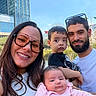 Valentina joined the competition — help win amazing prizes! family, selfie, child, baby, toddler, infant, adult, parents, group_portrait, smiling, outdoor, city, building, skyscraper, blue_sky, park, garden, sunglasses, beard, pink_outfit