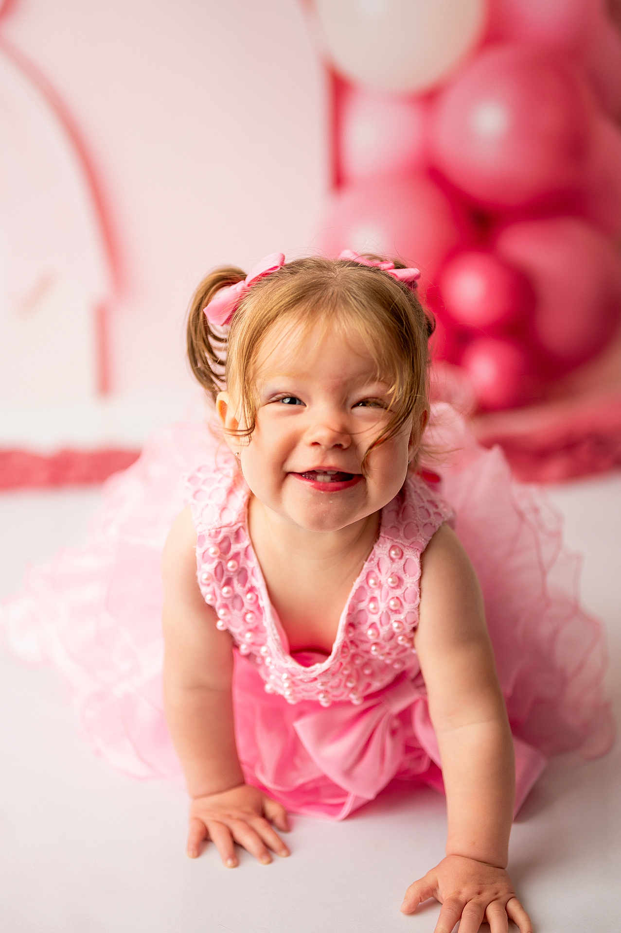 Claire joined the competition — help win amazing prizes! toddler, girl, pink_dress, pigtails, bows, smiling, crawling, balloons, pink_background, child, happy, portrait, cute, indoor, celebration, baby, closeup, playful, dress, person