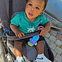 Hiram Treh a rejoint le concours — aidez-le/la à gagner de superbes lots ! toddler, child, stroller, outdoor, toy, sneakers, teal_shirt, curious, sunlight, pavement, cobblestone, hand, face, expression, playful, seat, baby_toy, footwear, person, summer