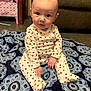 baby, infant, sitting, onesie, heart_pattern, blue_rug, blanket, living_room, sofa, toy_bin, portrait, hands, face, eyes, floor, cozy, indoor, cute, child, carpet