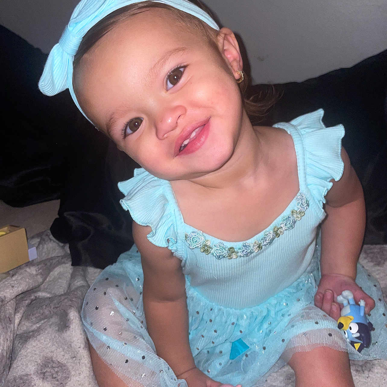 Jennaleigh is registered to the contest to win money with this photo: baby, blanket, blue_dress, child, clothing, cute, earrings, face, happy, headband, home, indoor, person, playtime, portrait, sitting, smiling, toddler, toy, young_child
