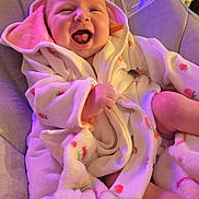 Lily joined the competition — help win amazing prizes! baby, infant, smiling, laughing, robe, carrot_pattern, cushion, seat, cozy, soft_lighting, indoors, child, happy, cute, face, skin, expression, clothing, blanket, comfort