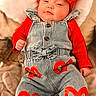 adorable, baby, casual, child, clothing, cozy, cute, denim_overalls, fashion, headwear, heart_pattern, indoors, infant, lying_down, pillow, portrait, red_bow, red_shirt, smiling, soft_texture