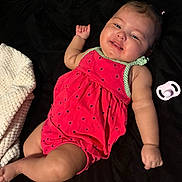 Emerald is registered to the contest to win money with this photo: baby, infant, smile, red_outfit, pigtails, pacifier, blanket, black_background, white_cloth, happy, cute, child, lying_down, skin, face, arm, leg, indoors, portrait, person