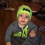 toddler, child, baby, batman, beanie, hat, nike, jacket, gray_clothing, floor, wood_floor, toy, cardboard_tube, furniture, indoor, person, face, hand, expression, living_room