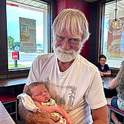Arizona joined the competition — help win amazing prizes! elderly_man, baby, restaurant, window, table, chair, blanket, white_tshirt, beard, smile, indoor, people, seated, nap, hand, glasses, light, poster, casual_clothing, wood