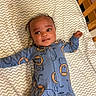baby, infant, onesie, blue_clothing, lion_pattern, blanket, chevron_pattern, bed, crib, child, cute, face, smile, lying_down, indoor, person, young_child, head, expression, comfortable
