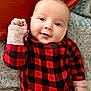 Beau is registered to the contest to win money with this photo: baby, infant, smile, face, eyes, hand, fist, red_clothing, checkered_pattern, blanket, bed, cozy, cute, portrait, child, young, indoors, soft_texture, warm_colors, happy
