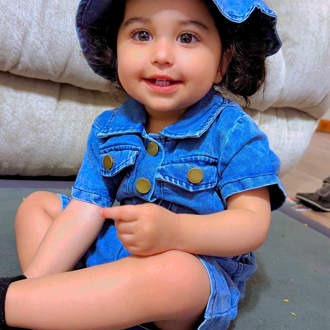 Jazleen is registered to the contest to win money with this photo: toddler, child, denim, hat, smiling, indoor, carpet, sitting, pointing, cute, happy, clothing, person, face, young_child, living_room, furniture, casual, portrait, baby