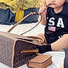 toddler, child, face, sitting, black_clothing, handbag, purse, curious, indoor, people, background, accessory, young_child, chewing, brown_bag, black_gloves, person, portrait, casual, cute