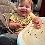 Ruby-Ann is registered to the contest to win money with this photo: baby, high_chair, smiling, winnie_the_pooh, food, messy, indoor, child, face, clothing, tray, person, happy, mess, hair, book_shelf, curtains, window, furniture, seat