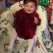 Ruby-Ann joined the competition — help win amazing prizes! baby, child, red_dress, headband, blanket, penguin_pattern, snowman_pattern, christmas_gifts, holiday, carpet, smiling, happy, indoor, cute, festive, tights, sitting, person, celebration, winter