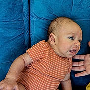 Kayson is registered to the contest to win money with this photo: baby, infant, child, onesie, orange_clothing, striped_clothing, blue_couch, furniture, hand, skin, face, expression, indoor, person, cute, young_child, seated, portrait, relaxing, home
