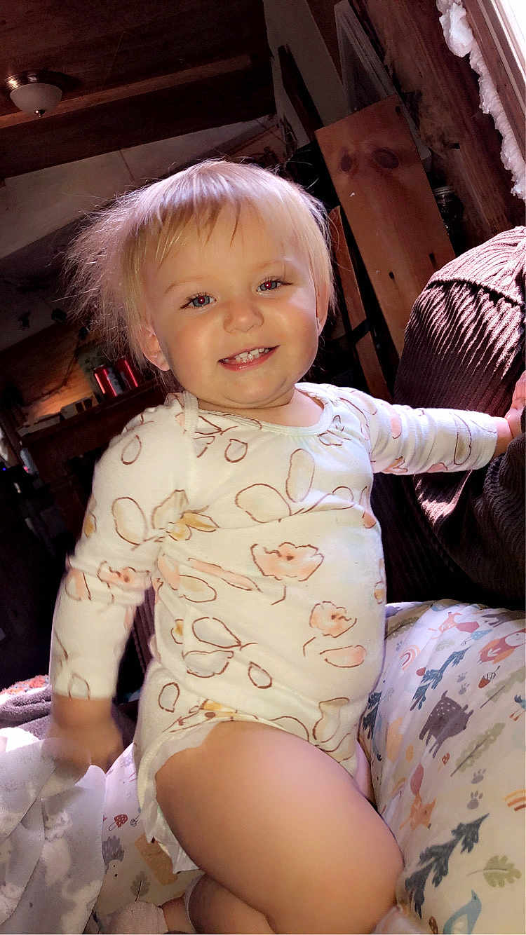Maevyn is registered to the contest to win money with this photo: toddler, child, smiling, blonde_hair, indoor, pajamas, cushion, patterned, wooden_furniture, cozy, warm_light, face, person, happy, cute, home, plush, sitting, blanket, young_child
