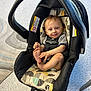 baby, car_seat, carrying_handle, child, clothing, diaper, fabric, floor, foot, hair, happy, indoor, light, patterned_cushion, person, playful, room, seatbelt, smile, toddler